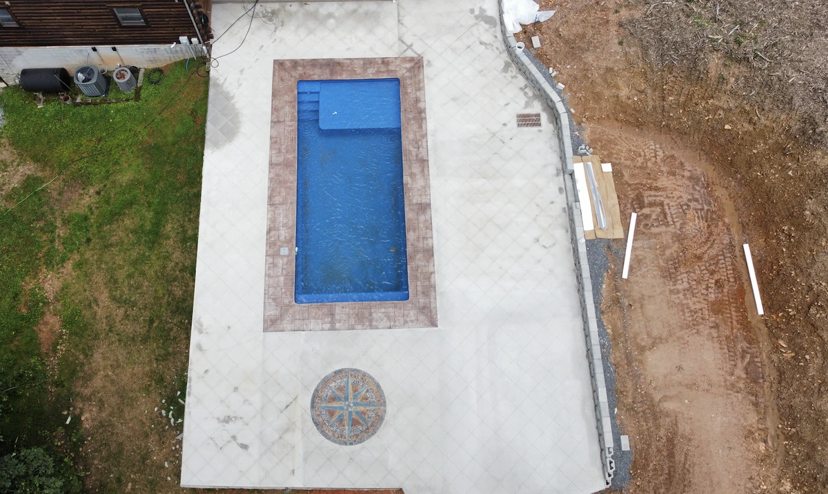 Aerial view of a rectangular pool ringed by stamped concrete coping and a wide scored pool deck with a compass rose medallion &mdash; The Foothills Concrete Company