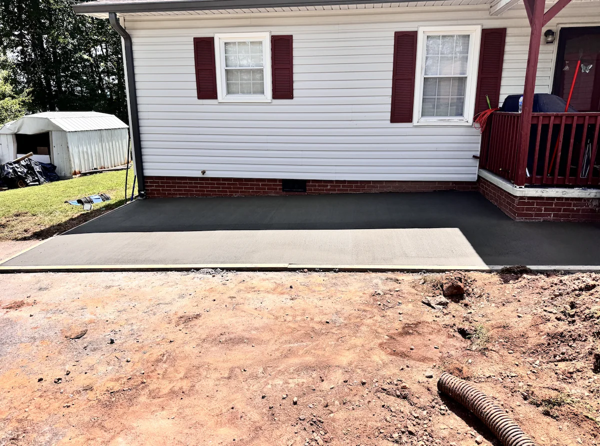 Freshly poured broom-finished concrete driveway extension beside a white ranch home, timber edge form still in place &mdash; The Foothills Concrete Company