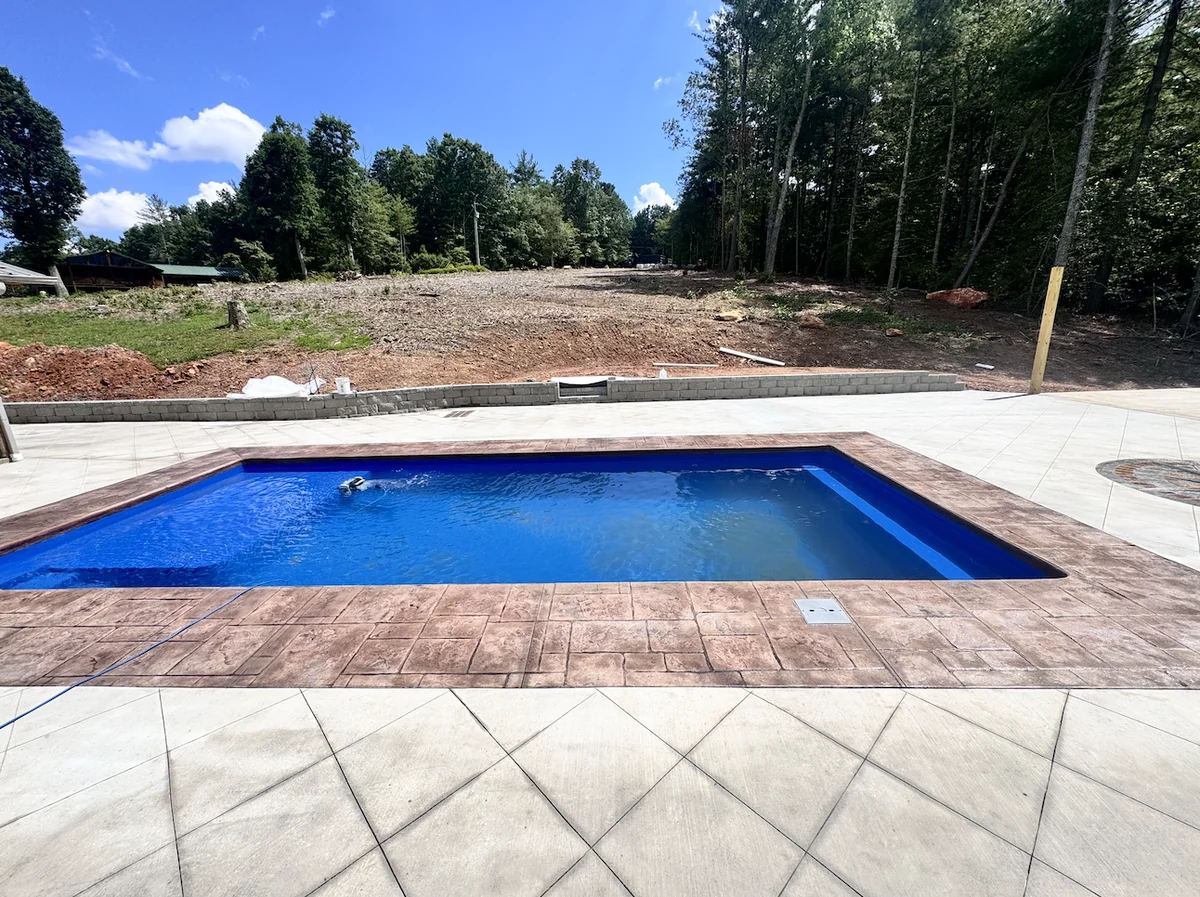 Rectangular pool with stamped concrete coping and a wide diamond-scored concrete pool deck at a newly cleared Foothills home site &mdash; The Foothills Concrete Company
